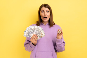 Portrait of shocked surprised woman holding bitcoin and big fan of dollar bills, exchange crypto...