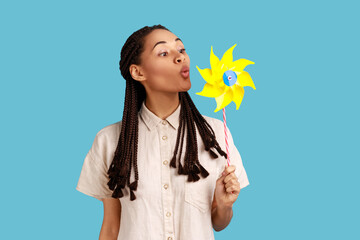 Pinwheel toy. Portrait of woman with black dreadlocks blowing at paper windmill, playing with hand...