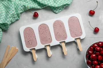 Cherry smoothie popsicles in reusable silicone ice pop mold or form on grey background. Making...