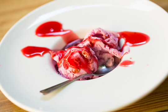 Two balls of pink ice cream with berry topping served on white plate..
