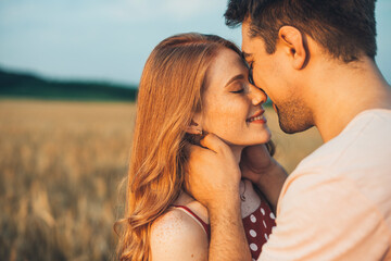 Portrait of a caucasian couple, man and woman, reach out close to each other for kiss. Standing in the wheat field. Love is in the air.