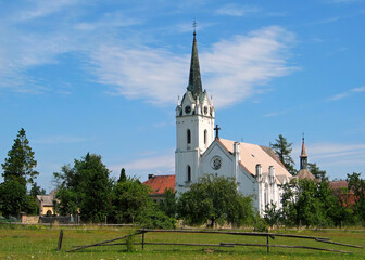Fototapeta na wymiar White country church with tower and clock. Village church with parish near cemetery, colorful background. Czechia.