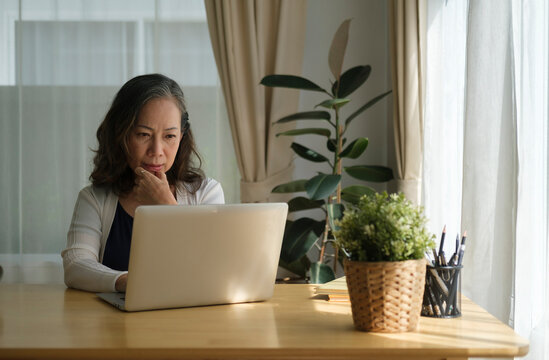 Senior Mature Woman Is Watching Business Training, Online Webinar On Laptop Computer While Remote Working From Home.