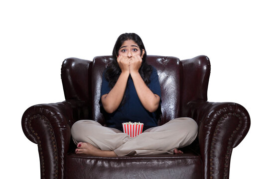 Asian woman with popcorn sitting on the couch with a scared expression