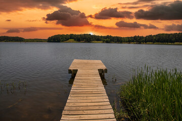Naklejka na ściany i meble a brown wooden dock over the rippling blue waters of Lake Acworth surrounded by lush green trees and blue with powerful clouds at sunset at Cauble Park in in Acworth Georgia USA