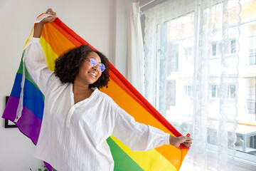 African American girl holding LGBTQ rainbow flag in her bed room for coming out of the closet and...
