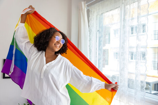 African American girl holding LGBTQ rainbow flag in her bed room for coming out of the closet and pride month celebration to promote sexual diversity and equality in homosexual orientation concept