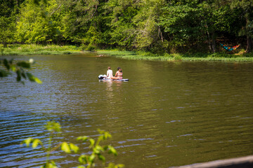 Fototapeta na wymiar two woman on a paddle board on the silky green waters of Lake Acworth surrounded by lush green trees and grass at Cauble Park in Acworth Georgia USA