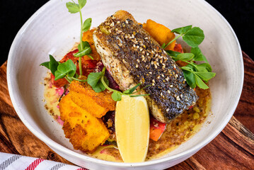 A serving of grilled barramundi fish with roast vegetables in a round white bowl