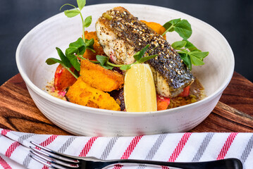 A serving of grilled barramundi fish with roast vegetables in a round white bowl