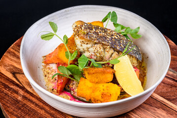 A serving of grilled barramundi fish with roast vegetables in a round white bowl