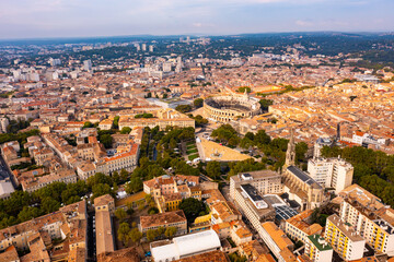 Fototapeta premium Drone view of ancient Roman amphitheatre Arena of Nimes on background of reddish tiled roofs of residential buildings on summer day, France