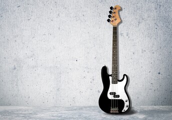 Electric guitar with wooden body and fret board stands the background of a wall.