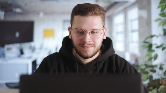 Young handsome man working on modern laptop while writing code for company application. Digital entrepreneur typing on keyboard and developing modern software in office space.