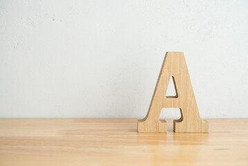 Wooden A alphabet letter on wooden table with white concrete wall background copy space. Top class,...