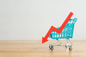 Shopping trolley with red chart falling down on wooden table background copy space. Economic recession crisis, core retail sales decrease, inflation or goods price up concept.