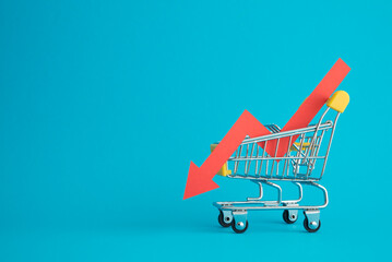 Shopping trolley with red chart falling down on blue background copy space. Economic recession crisis, core retail sales decrease, inflation or goods price up concept. - obrazy, fototapety, plakaty