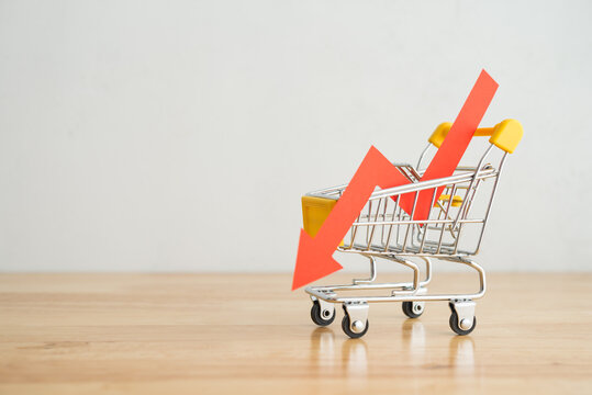 Shopping trolley with red chart falling down on wooden table background copy space. Economic recession crisis, core retail sales decrease, inflation or goods price up concept.
