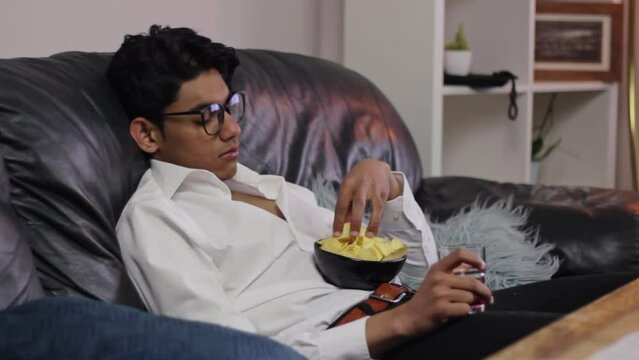 Hopeless demotivated young indian man eats junk food lying on couch, static