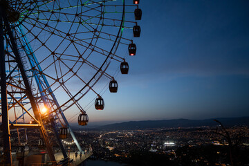 Famous ferris wheel in Mtatsminda amusement park in Tbilisi, Georgia, city and mountain on...