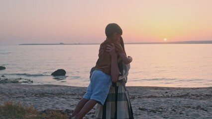 Happy cute affectionate mother hugs her beloved kid, son on walk in sea coast in summer. Little boy kid hugging mom outdoors in summer.