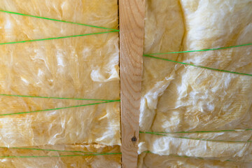 Glass roof insulation. Twine plastic thread supports the insulation between the rafters. Close-up of glass wool in yellow color