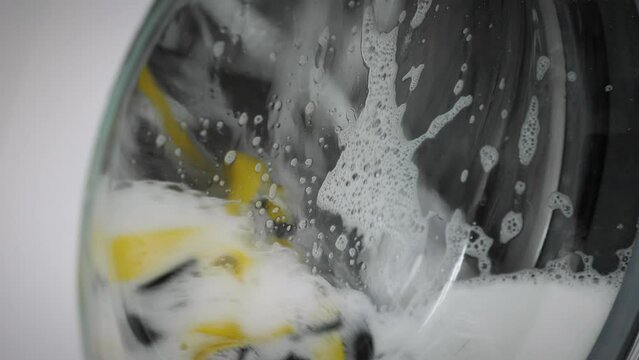 Washing machine cleaning clothes. Rotating colorful laundry and white soap foam