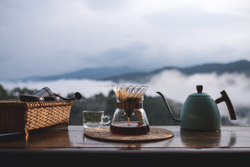 A set of coffee drip equipment on wooden balcony with mountain and nature view on foggy day