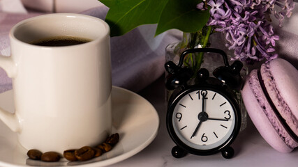 Obraz na płótnie Canvas Good morning. Morning cup of coffee. Lilac flowers and an alarm clock on a light background. Selective focus. 