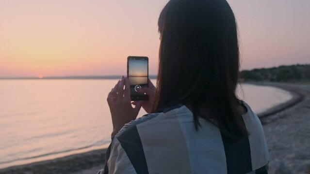 A beautiful girl photographs the dawn of the sun on the phone. The girl rejoices at the sunrise.