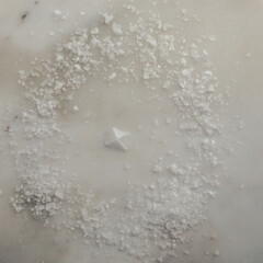 Maldon salt flakes with single pyramid shape salt crystal in center on white marble