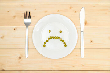 The concept of diet and anorexia. Green peas laid out on a white plate in the form of a sad smile....