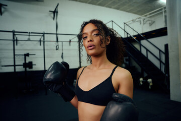 Fototapeta na wymiar African American female boxer training at the gym with boxing gloves on. Mixed race female holding boxing gloves in air. High quality photo