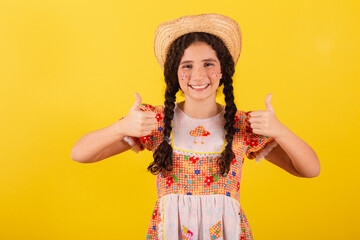 Girl wearing traditional orange clothes for festa junina. Thumb up, positive, affirmative. approval.
