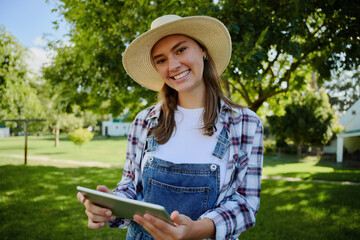 Caucasian female farmer wearing straw hat standing outdoors holding digital tablet 