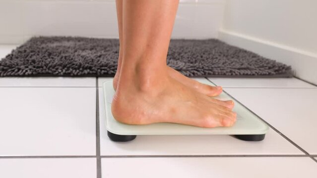 Woman checking her weight by stepping onto a bathroom scale.