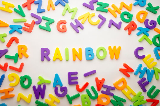 Rainbow word formed with colored letters on white background. Loose colored plastic letters forming word rainbow.