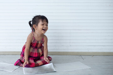 Funny kid in pink dress sitting and playing over white wall, little pretty girl