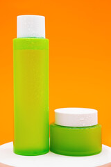 Set of green cosmetic bottle and jar on white podium against orange background. Summer collection skin care product.