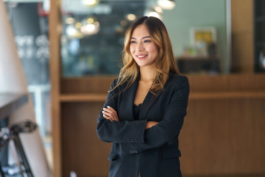 Beautiful Smiling Asian Businesswoman Standing With Arms Crossed In Office Looking Out Of The Window.