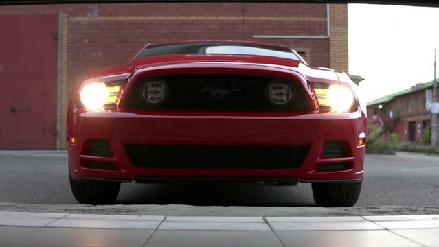 Red, luxury, sport, muscle car in front of garage gates. Revealing racing automobile with turned on headlights.