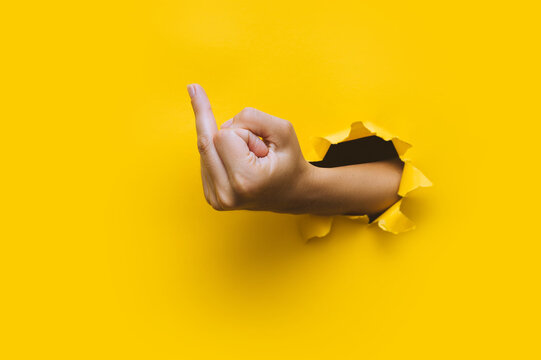 Middle finger, insulting gesture. Torn hole in yellow paper. Fuck you concept. Aggressive reaction.