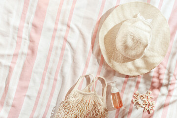 Summer pastel background with wide-brimmed sun hat, cosmetics products on striped beach towel as...
