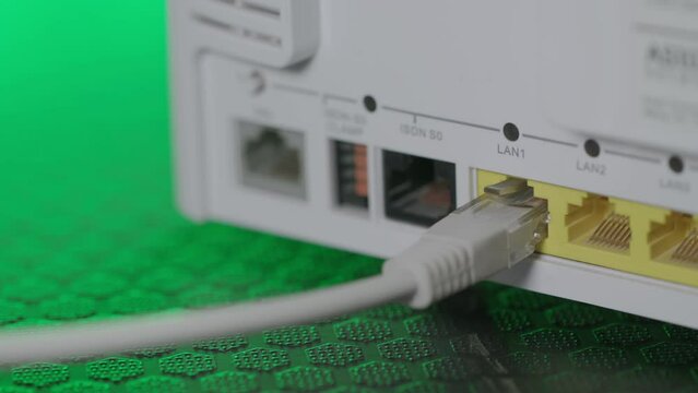 Close up shot of a man installing Ethernet network Patch Cable on router with colorful light in the background. Wireless Router On The Desk.