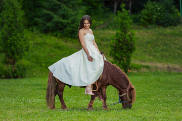 girl in a white dress rides a pony on a green lawn