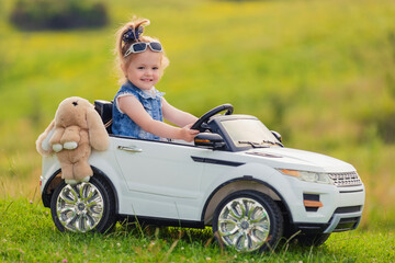 little girl rides on a children's car on a green lawn