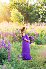 beautiful pregnant girl in a purple dress is picking flowers in a field of lupines. A woman with a bouquet of purple flowers