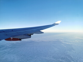 Fototapeta premium View from the porthole on the wing of an airplane with a red aircraft engine flying above beautiful white clouds.