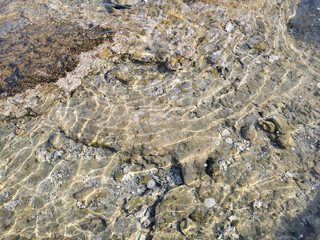 The coast of the Mediterranean Sea, clear water with reflections of the sun's rays, through which you can see the stone bottom. Background.