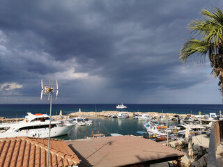 Fototapeta na wymiar Pier, port with small ships, yachts and boats in the bay of the Mediterranean Sea against the backdrop of a dramatic sky.